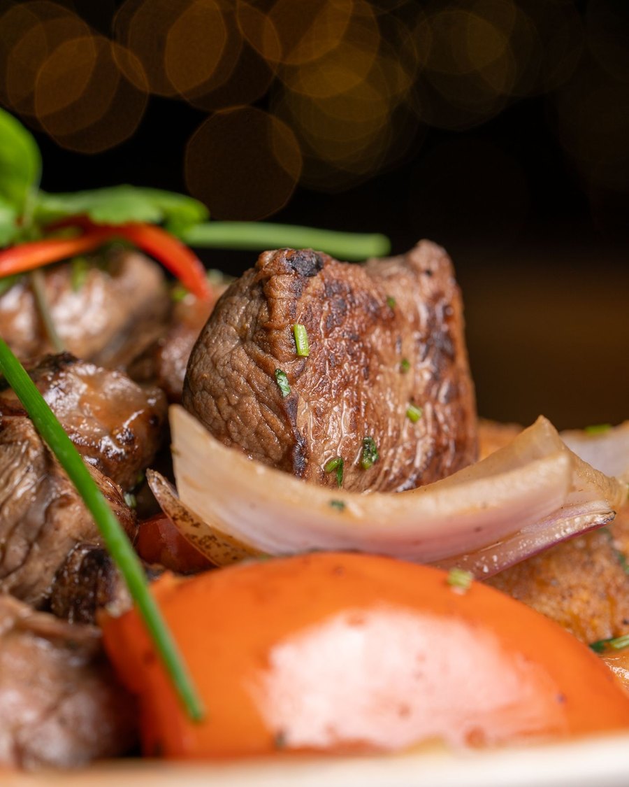 Licensed stock photograph: pieces of grilled beef with charred onion and roasted vegetables.