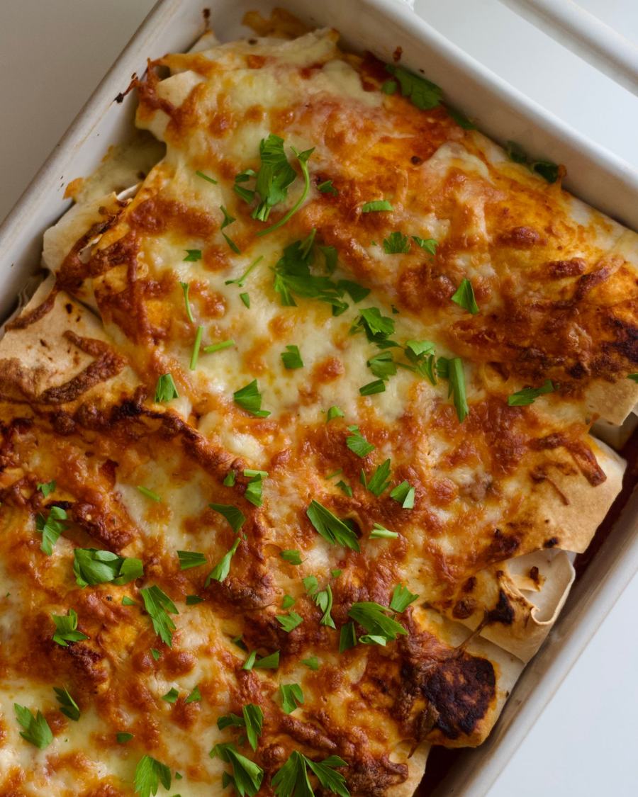 Licensed stock photograph: enchiladas baked under melted cheese and scattered with fresh herbs.