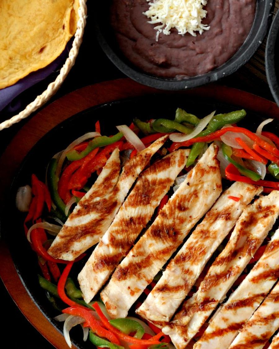 Licensed stock photograph: grilled fajita strips with red and green peppers, tortillas, beans and guacamole.