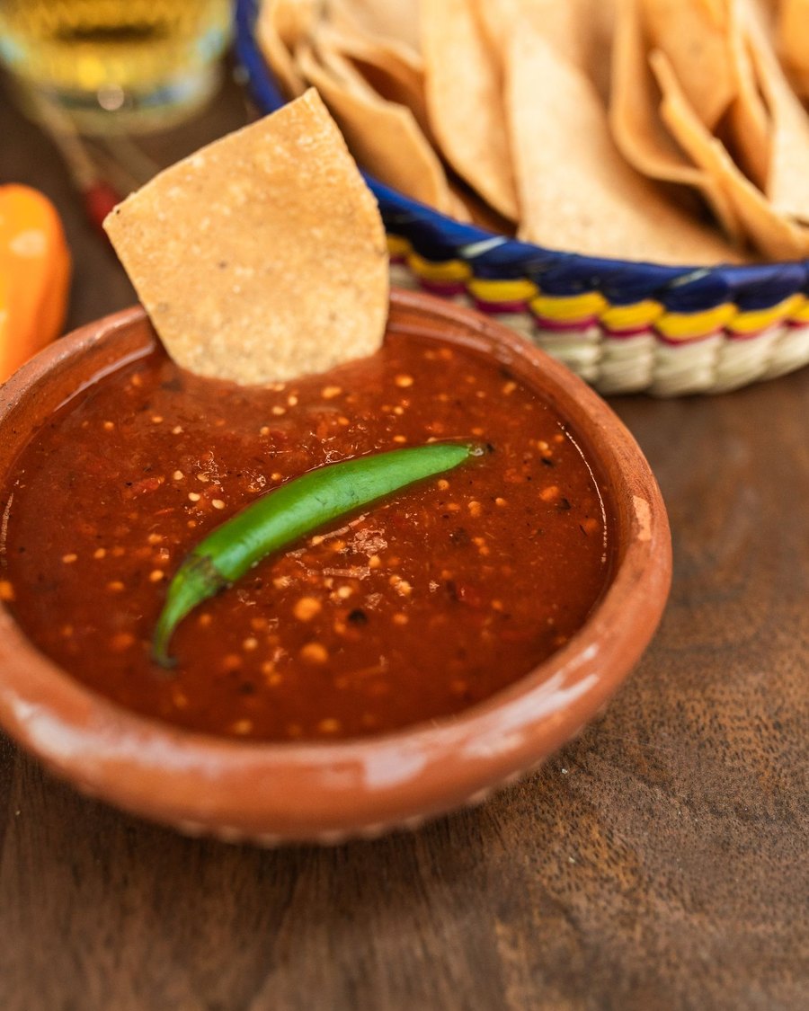 Licensed stock photograph: red salsa in a clay bowl with a green serrano pepper and a tortilla chip.